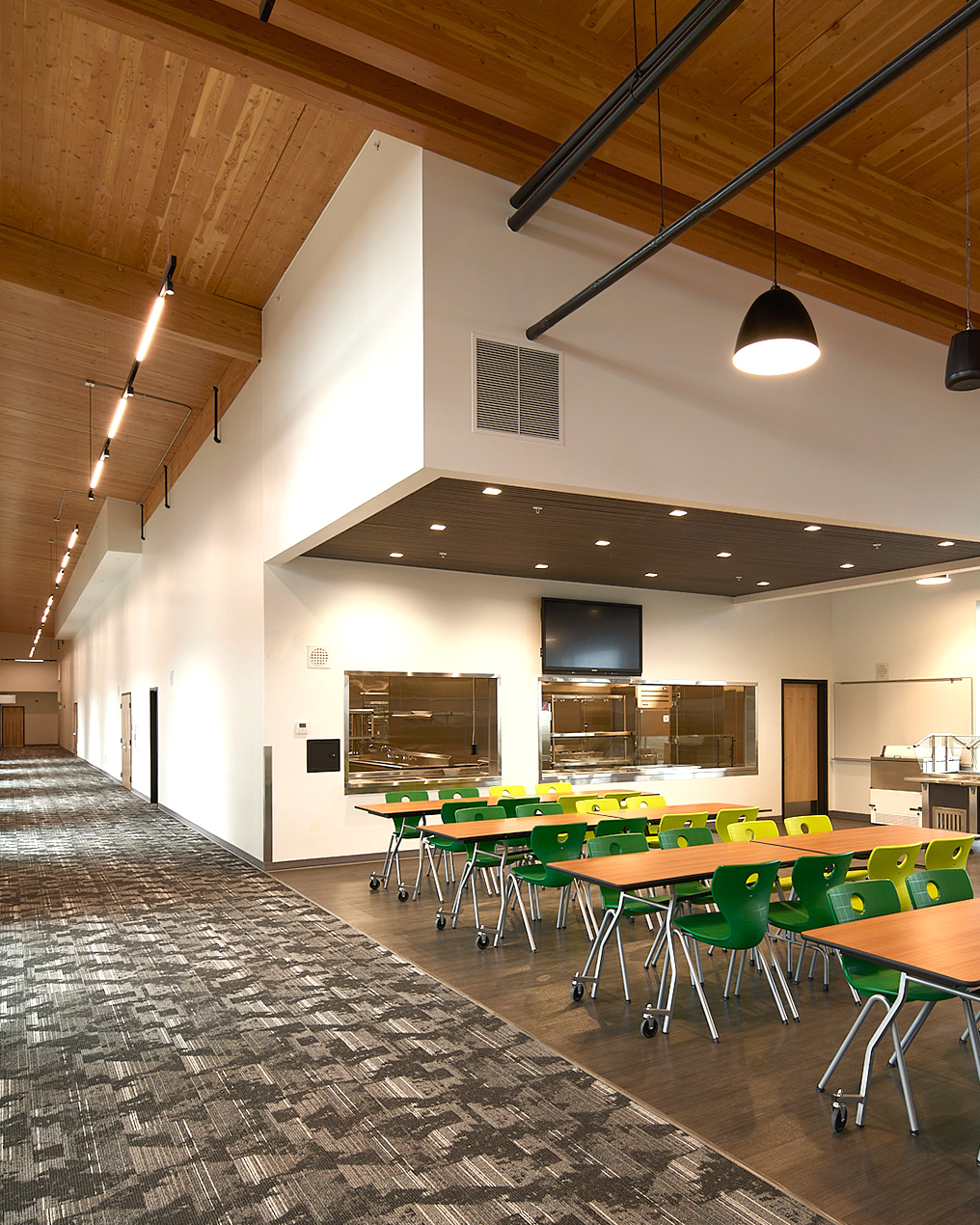 Mass timber school cafeteria interior with exposed wood ceiling and structural beams